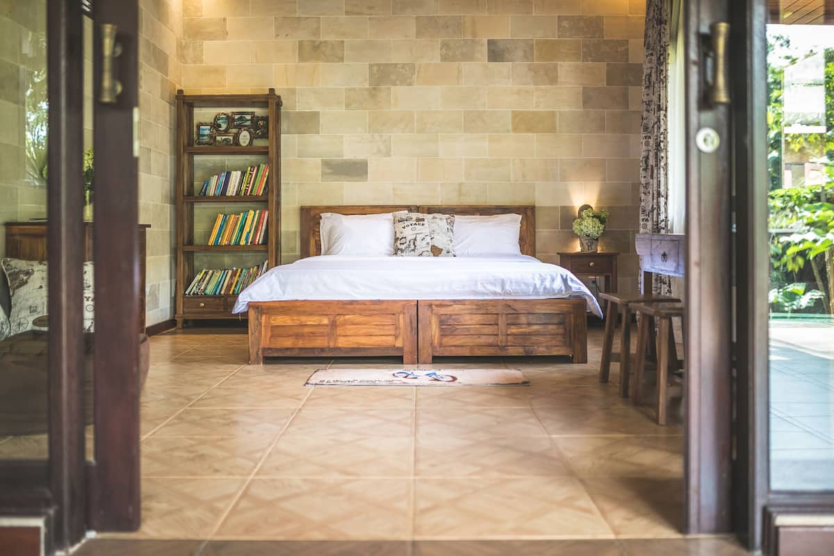 A bedroom with a wooden bed, a bookshelf, and a view of the outdoors.