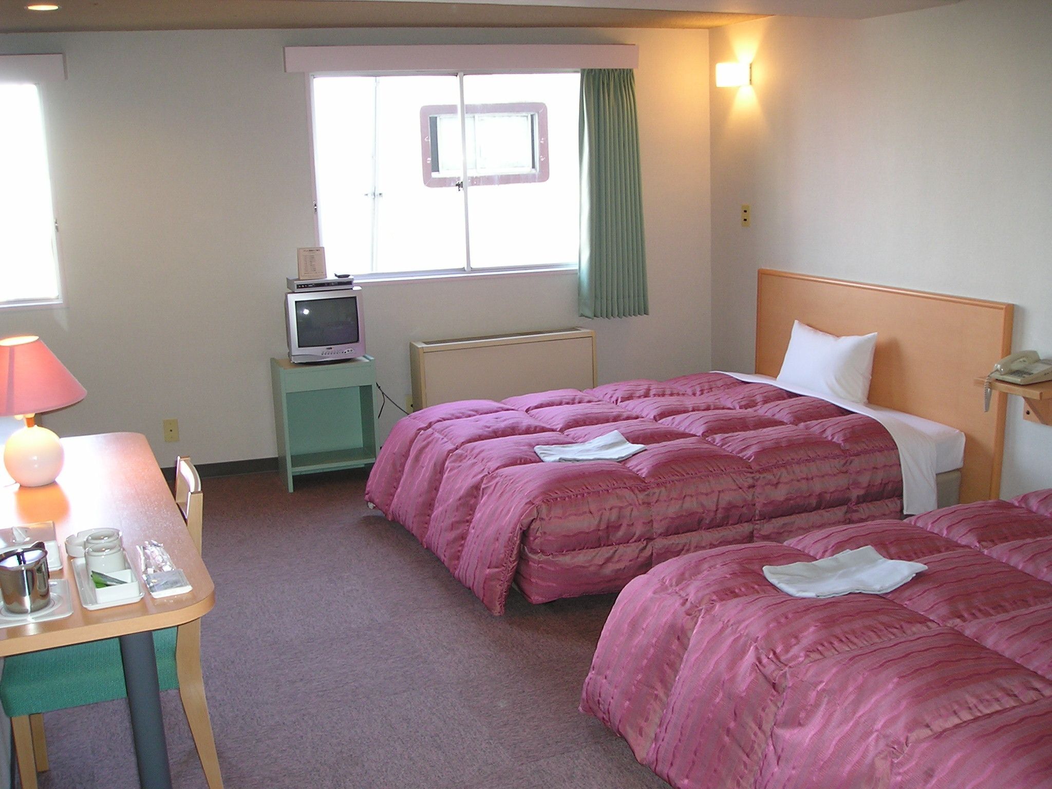 Une chambre d’hôtel avec deux lits, une petite table avec une lampe, un téléviseur posé sur une table d’appoint et une fenêtre avec des rideaux.