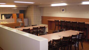 A conference room with a long table and chairs, a kitchenette area, and a whiteboard on the wall.