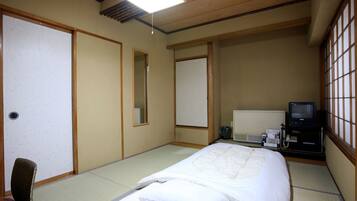 A traditional Japanese-style hotel room with tatami flooring, a bed with white bedding, a television, and a desk with a computer.