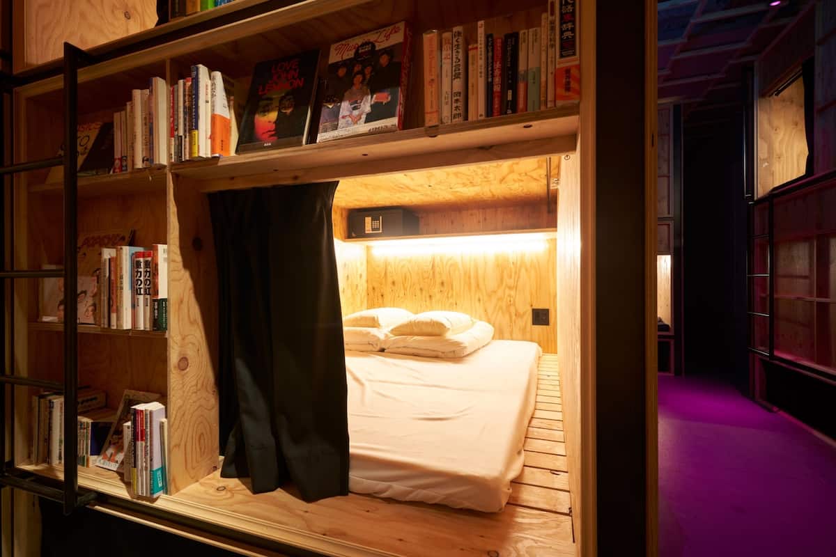 A wooden bunk bed with a bookshelf above it, containing books and a framed picture.