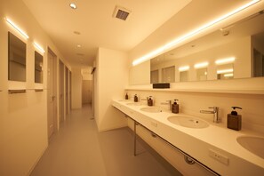 Un baño moderno con tres lavamanos, un espejo grande e iluminación en el techo.