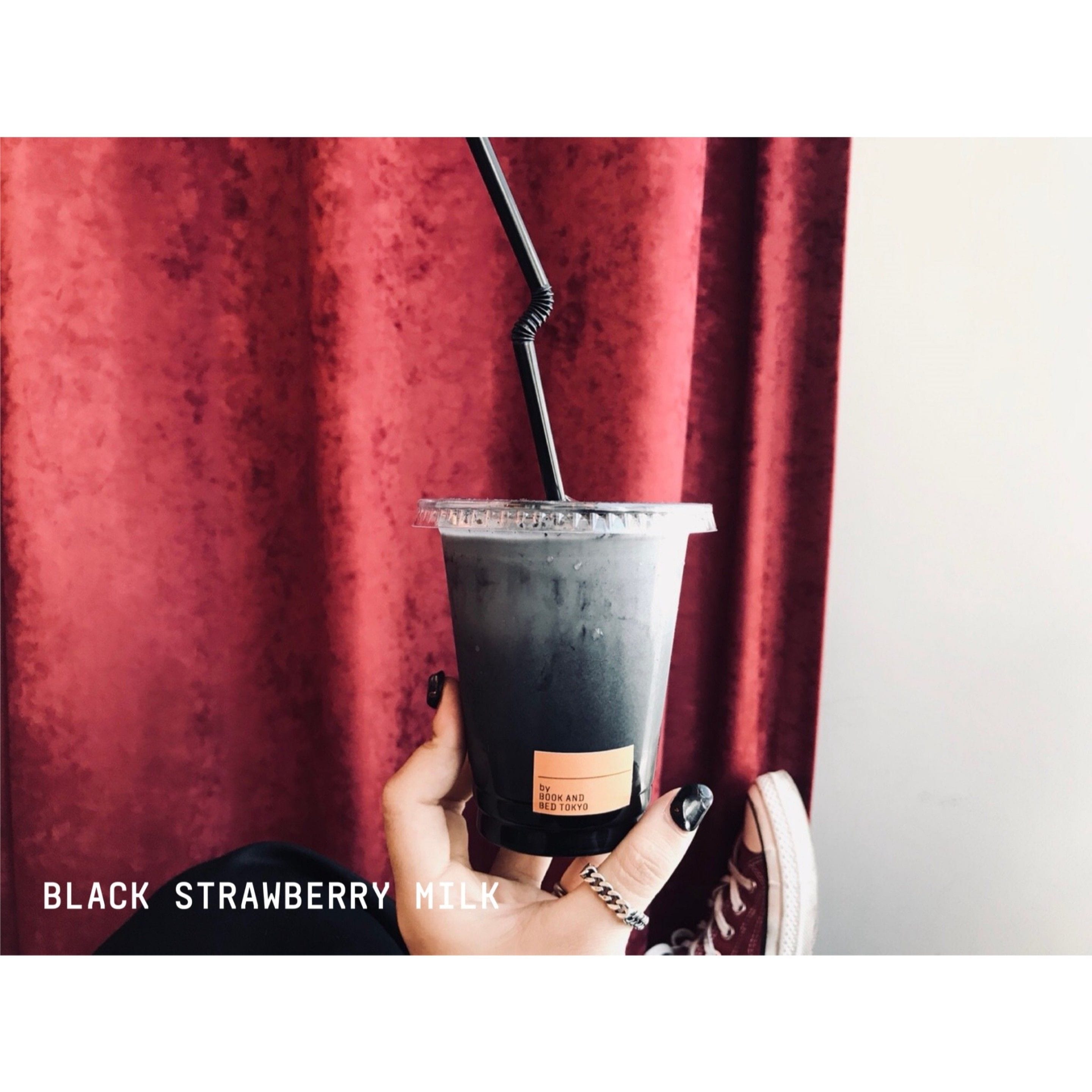 Une main tenant un gobelet noir en plastique avec une étiquette indiquant « LAIT À LA FRAISE NOIRE ».