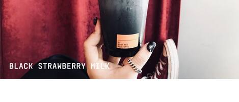 A hand holding a black straw cup with a label reading "BLACK STRAWBERRY MILK".