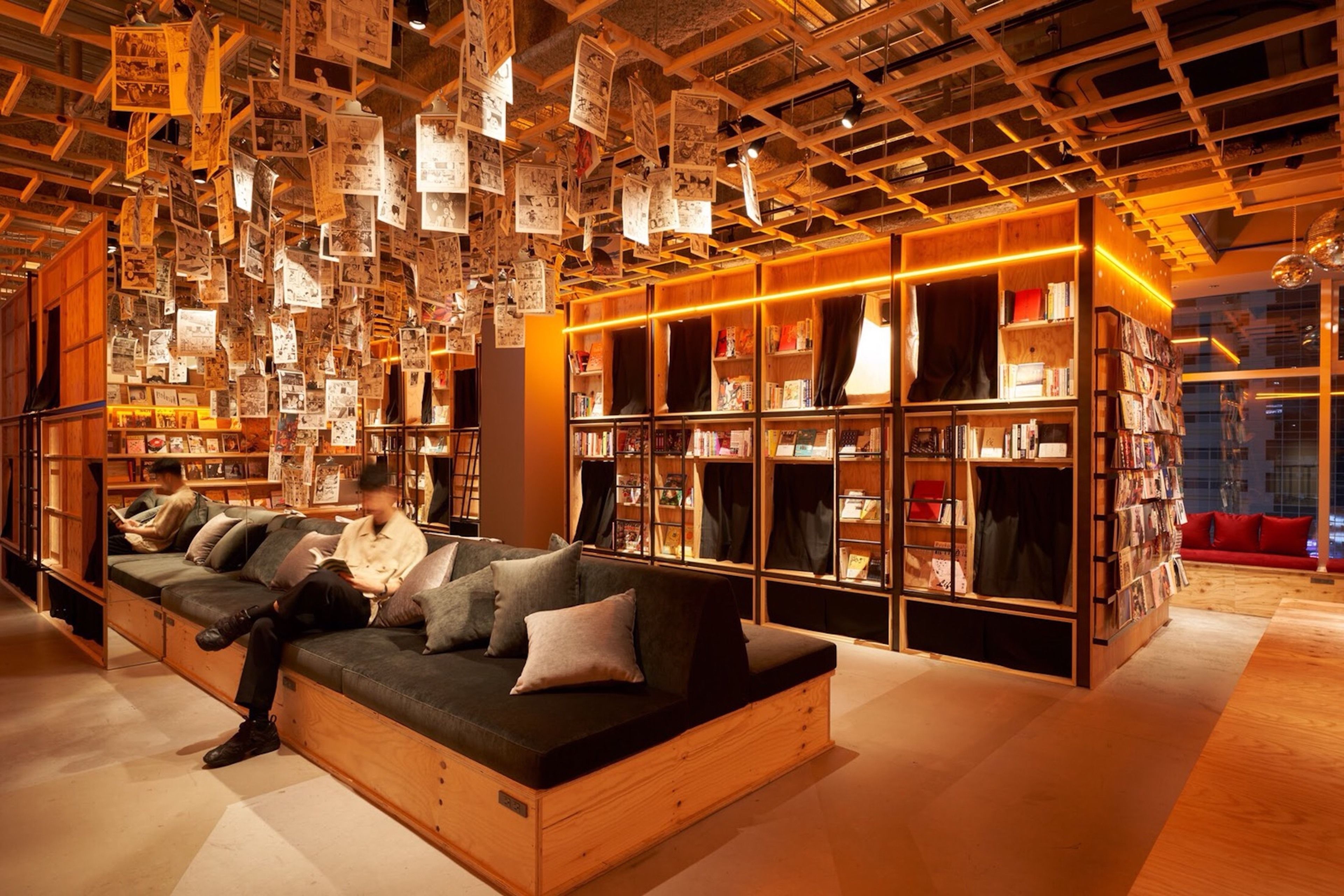 A modern library with a wooden sofa, bookshelves, and hanging papers.