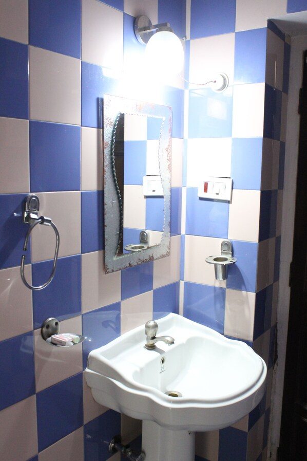 A bathroom with a white sink, a mirror, and blue and white checkered tiles. - Kunjpur Guest House (Prayagraj)