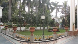 Un patio con un reloj, palmeras y macizos de flores.