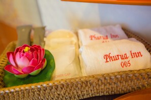 A wicker basket containing a pink lotus flower, a shower cap, and two towels with 'Phurua Inn 005' embroidered on them.