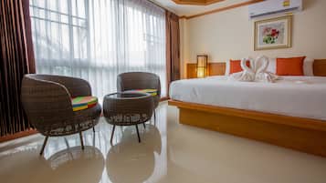 Habitación de hotel con una cama grande, dos sillones de mimbre, una mesita y un ventanal con cortinas.