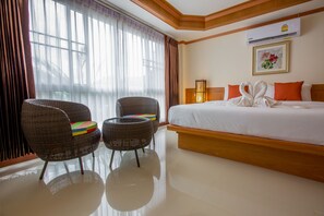 A hotel room with a large bed, two wicker chairs, a small table, and a window with curtains.