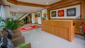 A spacious lobby with a wooden reception desk, a red carpet, and a staircase leading to an upper floor. - Phurua Inn (Phu Ruea)