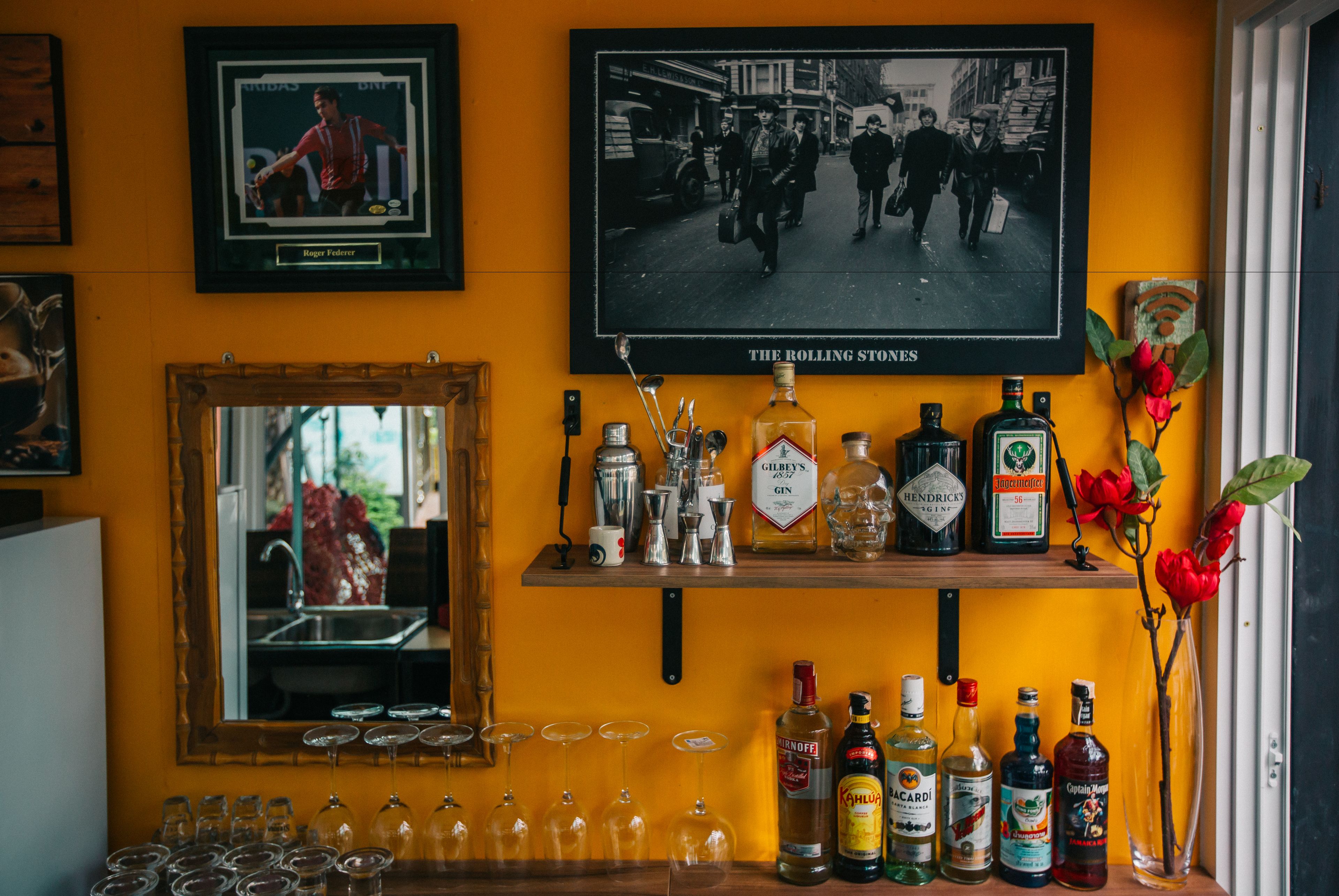 Un coin bar avec une étagère remplie de bouteilles d’alcool, de verres et une photo encadrée représentant une scène de rue d’époque.