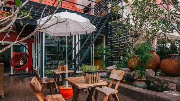 A wooden outdoor seating area with tables and chairs, a white umbrella, and potted plants. - Phurua Inn (Phu Ruea)