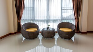A room with three wicker chairs and a small round table, a window with sheer curtains, and a view of the outside. - Phurua Inn (Phu Ruea)
