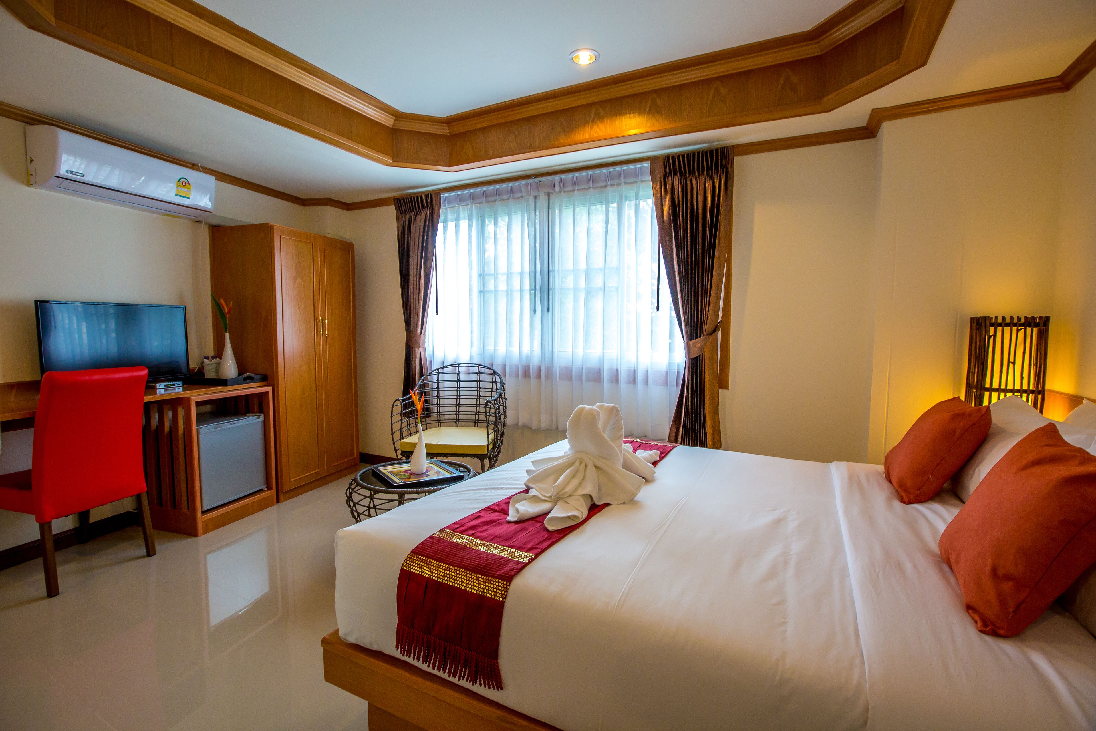 A hotel room with a bed, a desk, a chair, an air conditioner, and a window with curtains.
