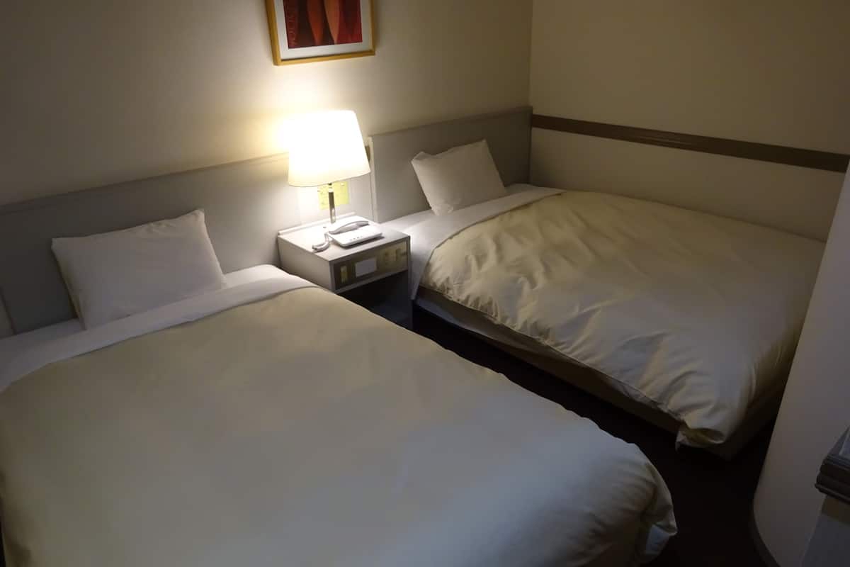 A hotel room with two single beds, a bedside table with a lamp, and a telephone.