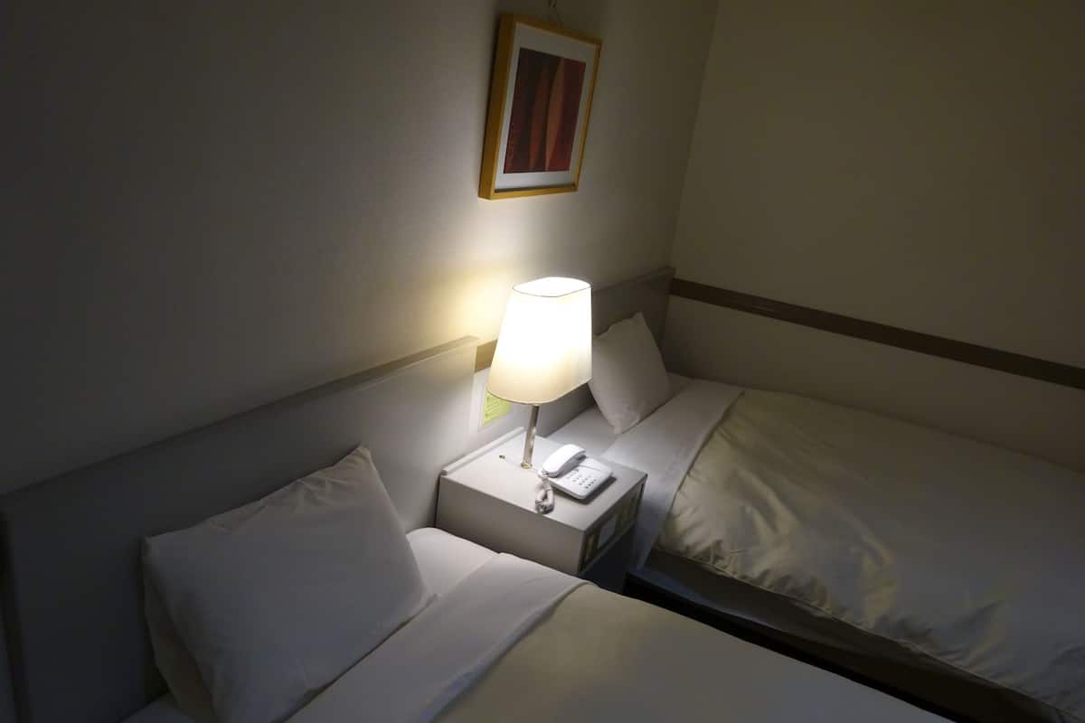 A hotel room with a bed, a bedside table with a lamp, and a framed picture on the wall.