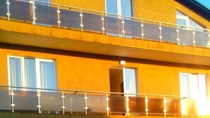 A multi-story building with a yellow facade, balconies with glass railings, and a small garden area in front.