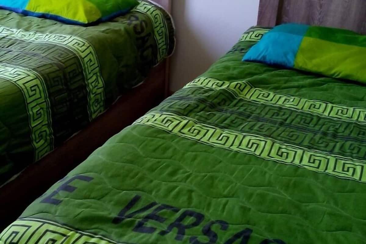 Dos camas individuales con cabeceros de madera y ropa de cama verde con estampado geométrico.