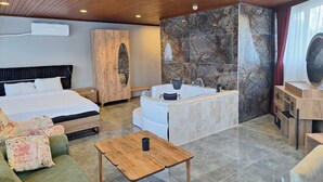 Una moderna camera d'albergo con un letto grande, un'area salotto con un divano verde, un tavolino in legno, una parete in pietra e una vasca da bagno.