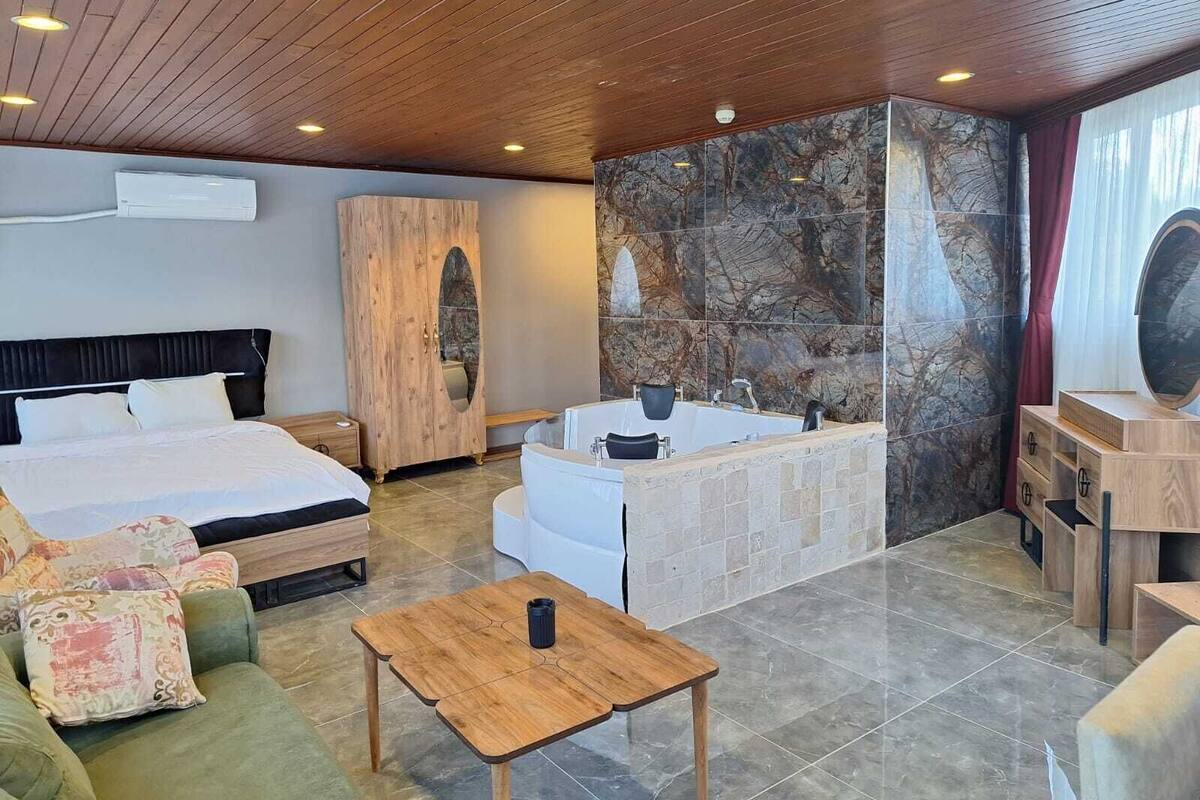 Une chambre d’hôtel moderne dotée d’un grand lit, d’un coin salon avec un canapé vert, d’une table basse en bois, d’un mur en pierre et d’une baignoire.