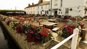 A riverside pub with outdoor seating and flower boxes.