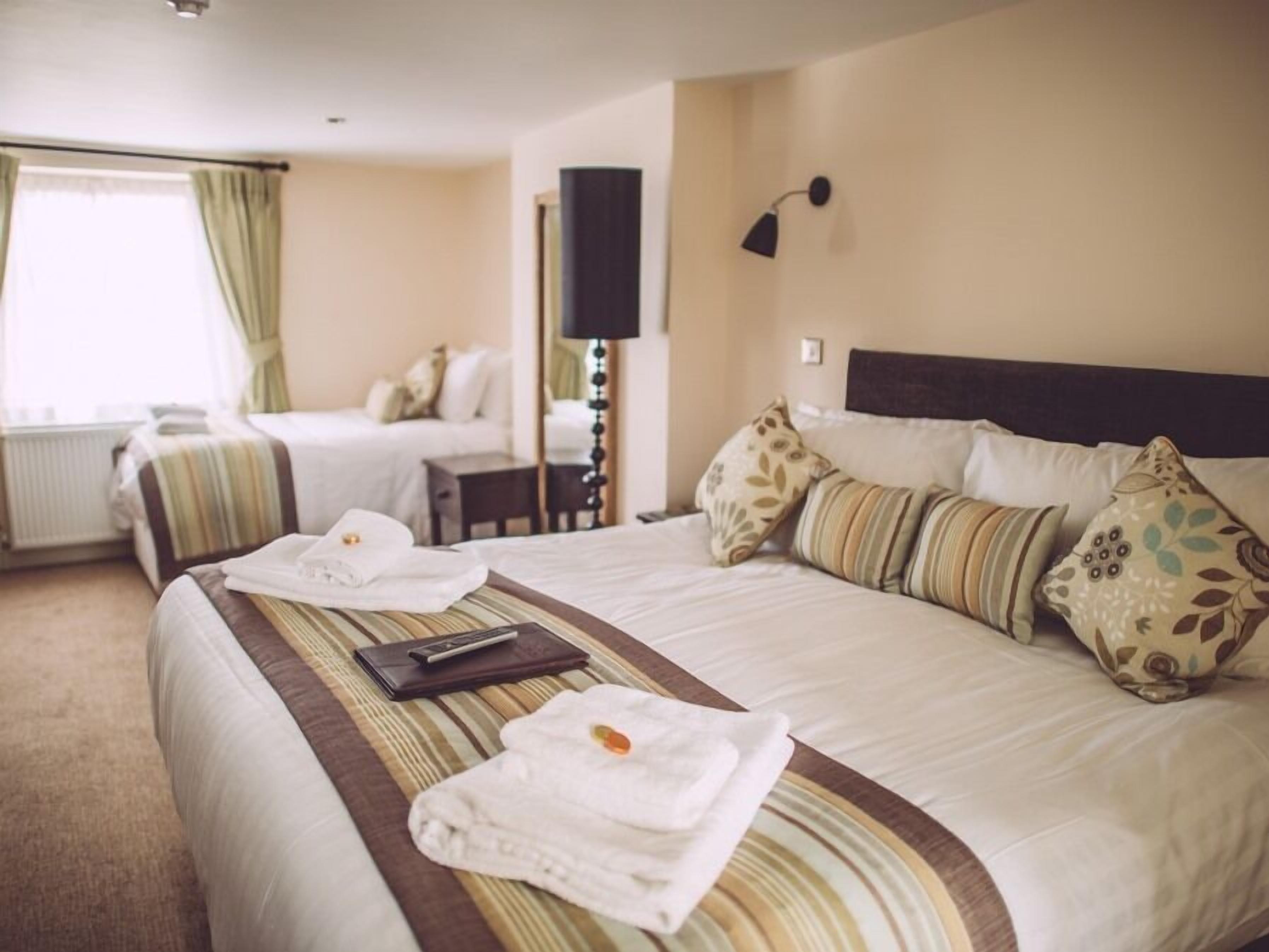 A hotel room with two beds, a bedside table, a lamp, and a window with curtains.