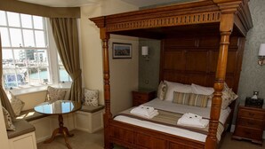 A four-poster bed with a wooden frame, a small round table, and a bench by the window.