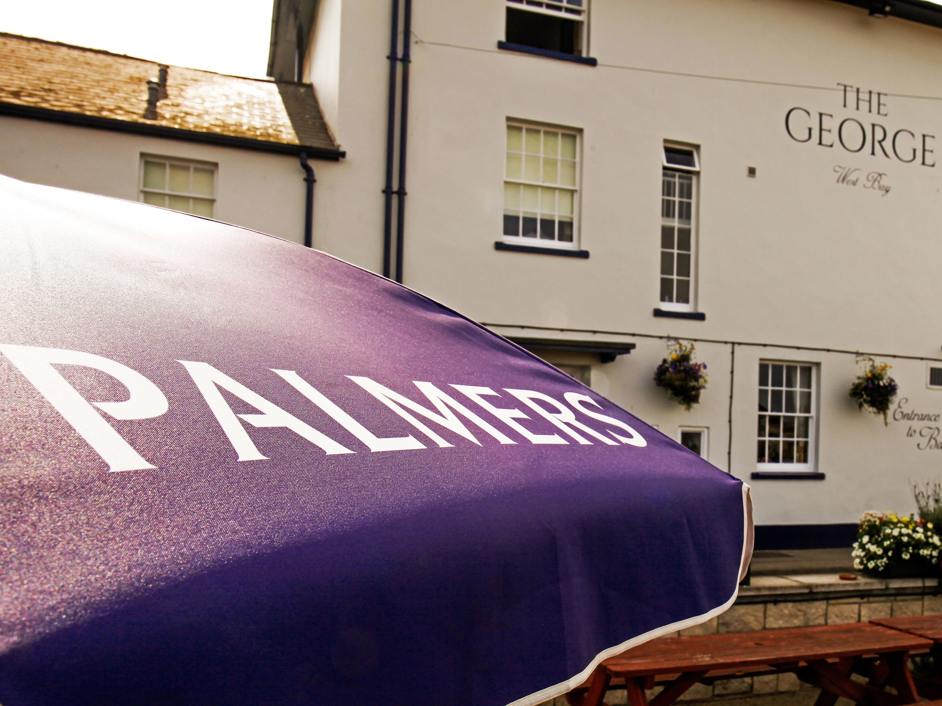 A purple umbrella with "PALMERS" written on it, in front of a building with "THE GEORGE" written on the wall.