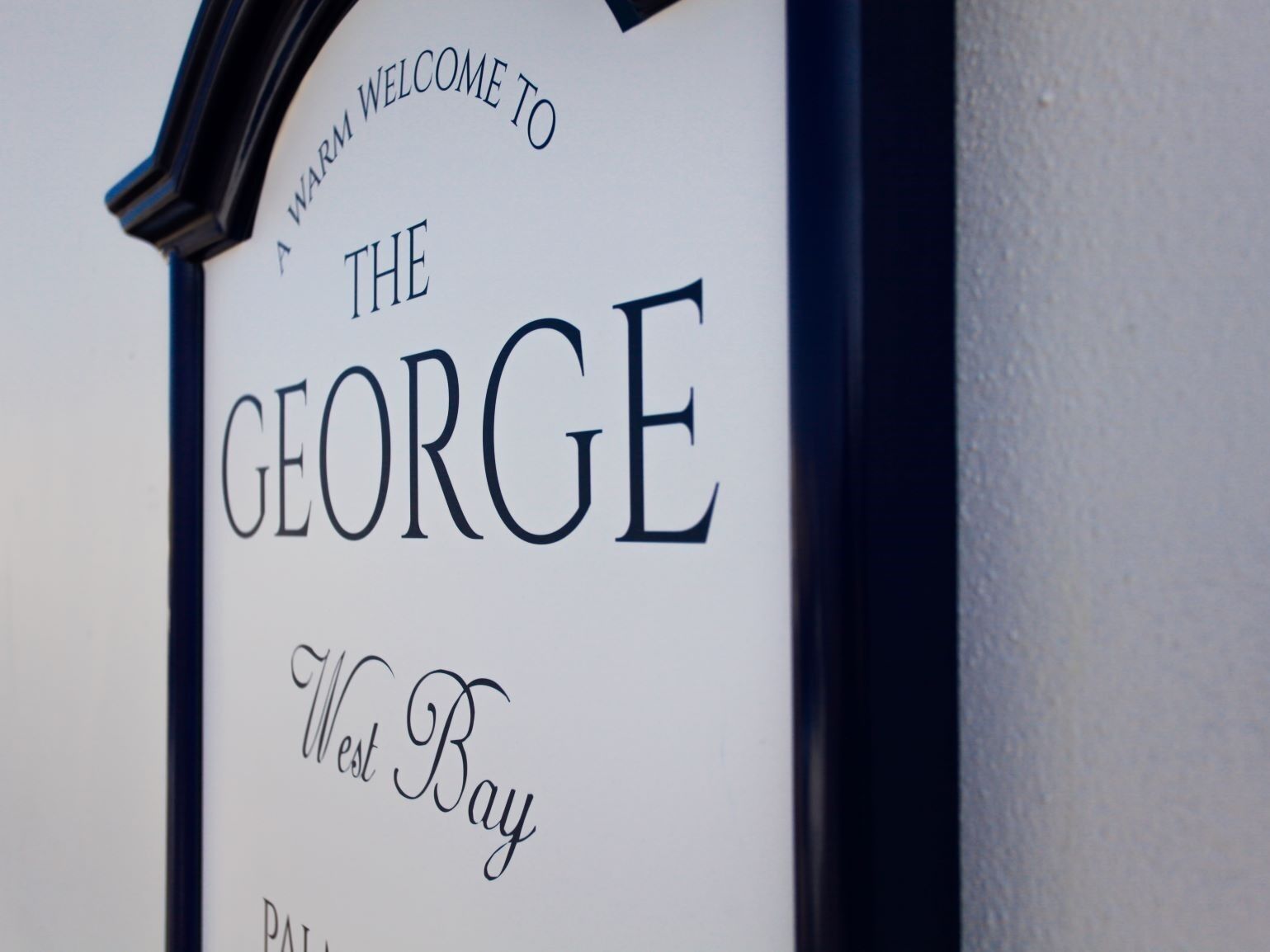 A sign with the text "A WARM WELCOME TO THE GEORGE West Bay."