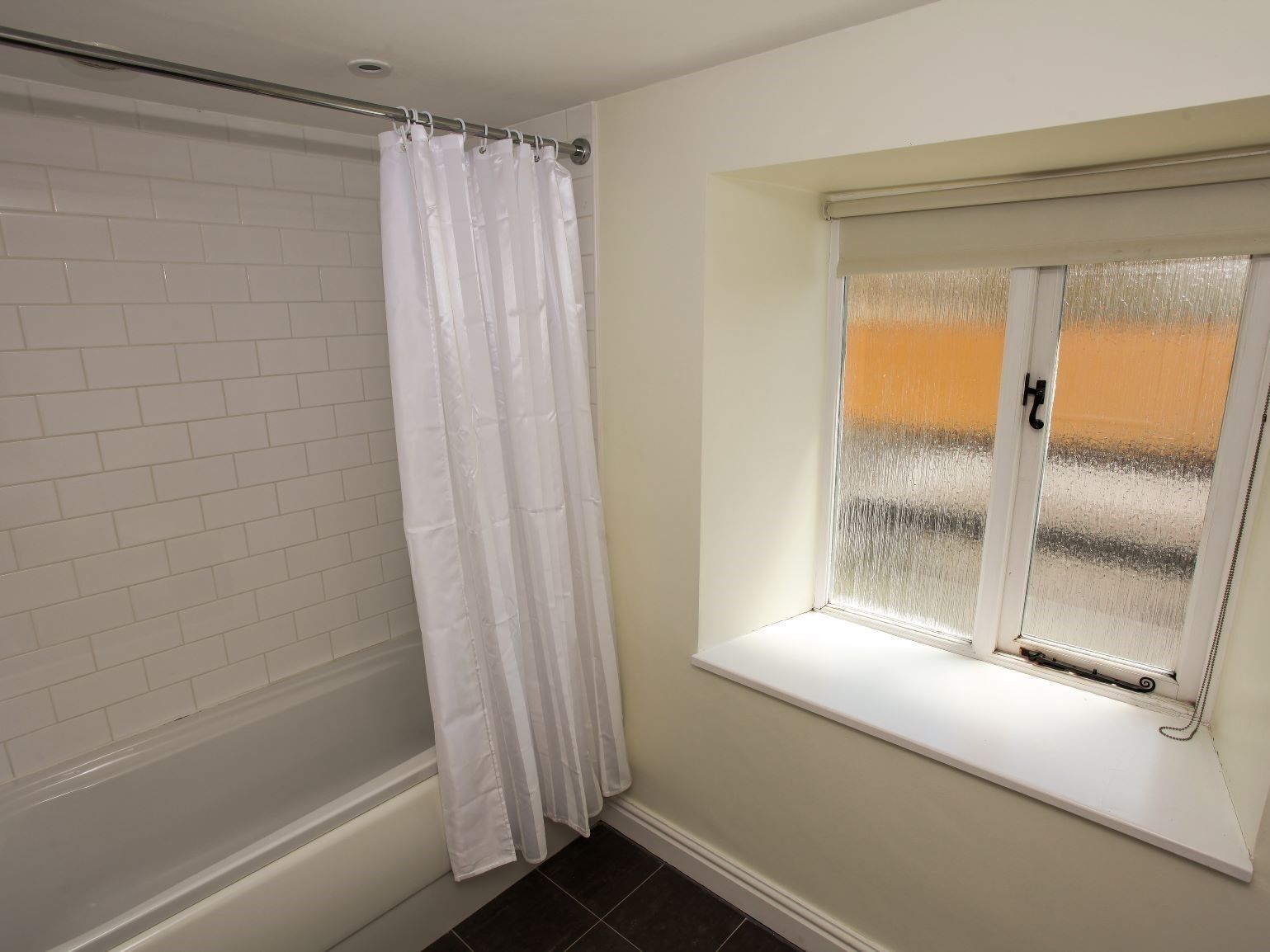 Une salle de bain avec une baignoire, un rideau de douche blanc et une fenêtre à vitres dépolies.