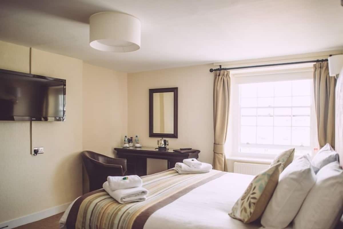 A hotel room with a bed, a desk, a chair, a television, a mirror, and a window with curtains.