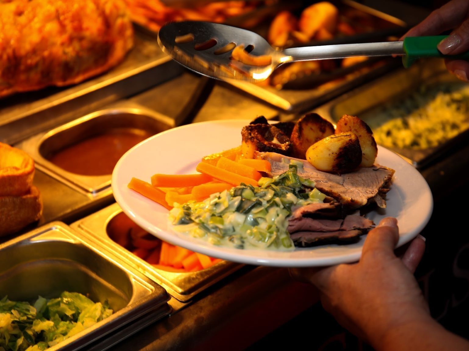 A buffet with various dishes including roasted potatoes, carrots, and a meat dish, served on a white plate.