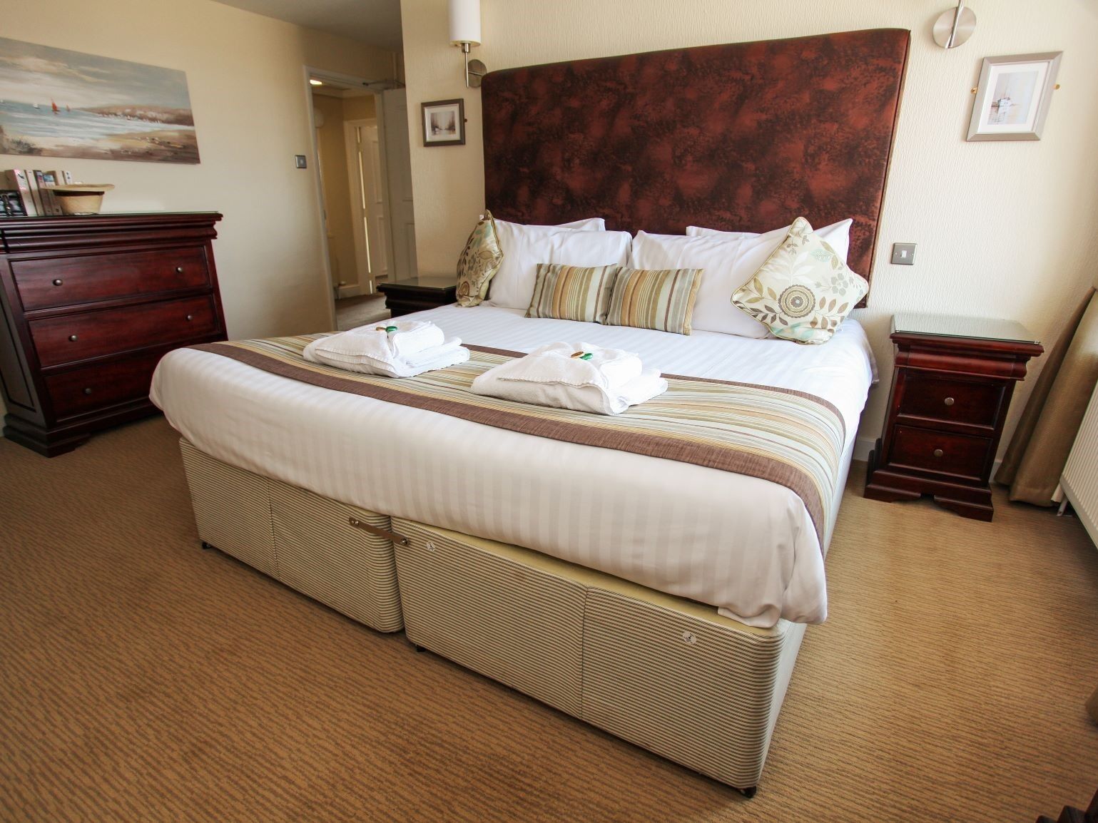 A hotel room with a large bed, a wooden headboard, a bedside table, a nightstand, and a wall-mounted lamp.