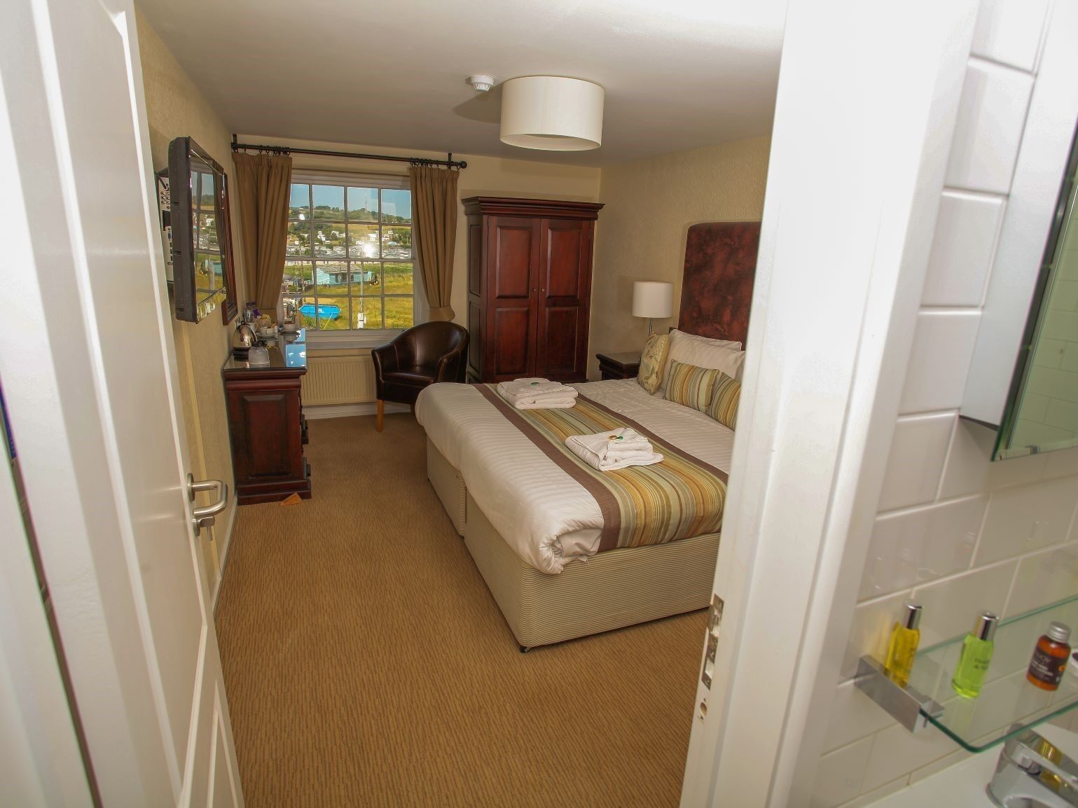 A hotel room with a bed, a desk, a chair, a window with a view, and a bathroom with toiletries.