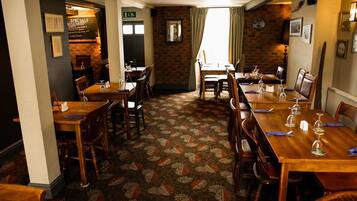 A restaurant with wooden tables and chairs, a patterned carpet, and brick walls.