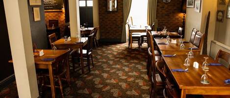 Un restaurante con mesas y sillas de madera, alfombra estampada y paredes de ladrillo.