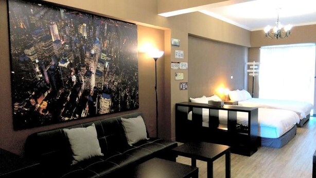 A hotel room with a large cityscape painting, a bed with white linens, a black sofa, and a desk with a lamp. - Summer Kenting B&B (Hengchun)