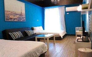Habitación con dos camas, un sofá, una mesa, una araña, una ventana con cortinas y un aire acondicionado instalado en la pared.