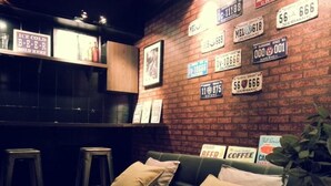 A cozy bar area with a brick wall adorned with license plates and a green couch with cushions. - Summer Kenting B&B (Hengchun)