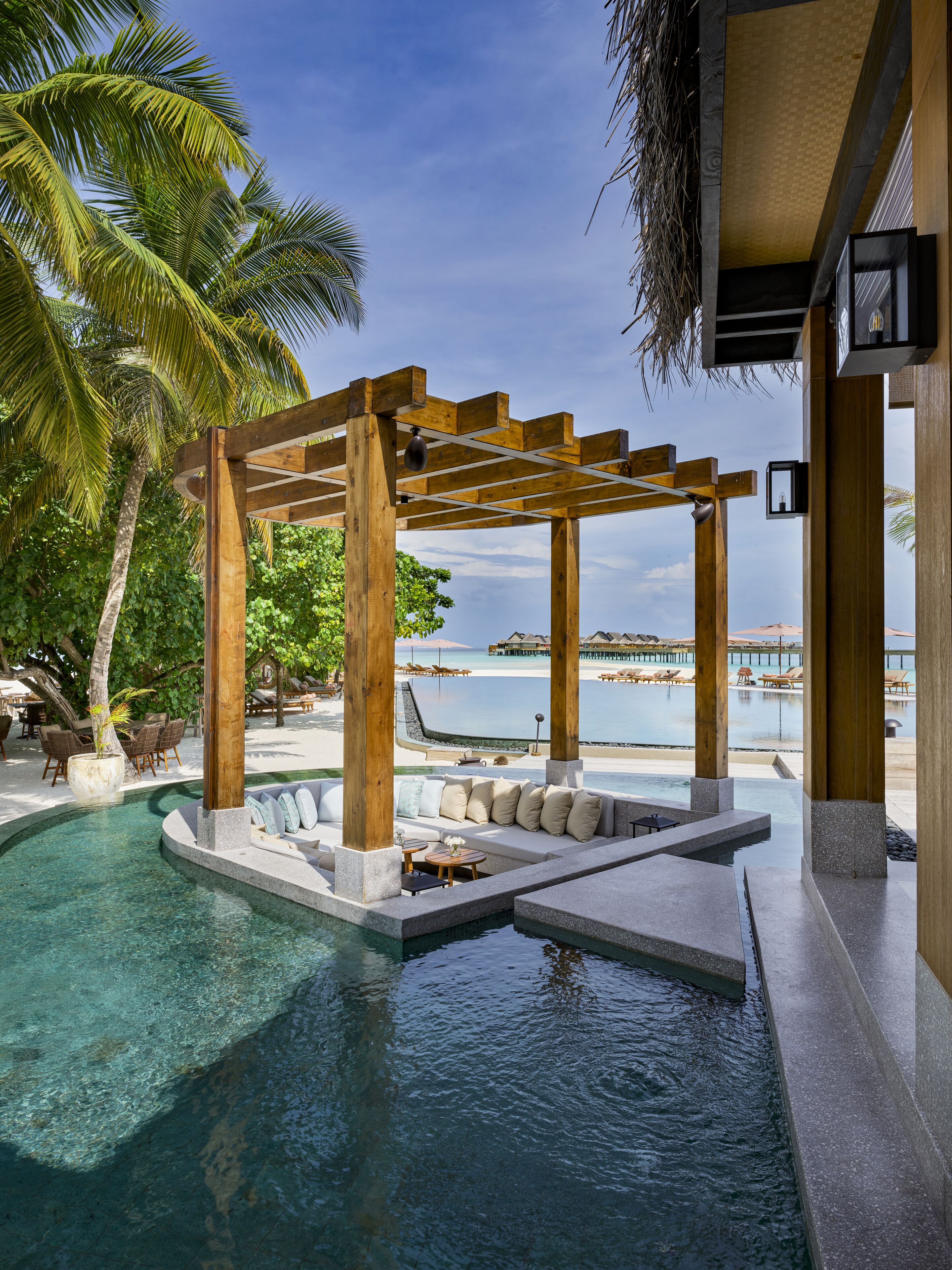 Zona de piscina con un porche de madera, asientos y vistas al mar.