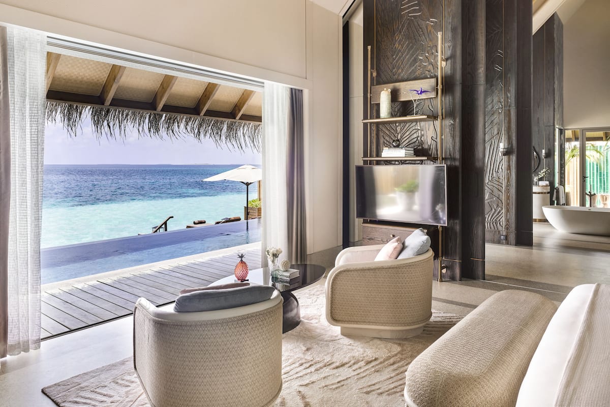 A modern living room with a view of the ocean, a pool, and a tropical setting.