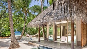 A poolside area with a thatched-roof structure, palm trees, and a clear view of the ocean. - JOALI Maldives (Muravandhoo)