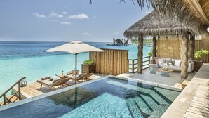 An infinity pool with clear blue water, wooden deck, lounge chairs, and a thatched-roof structure with a view of the ocean. - JOALI Maldives (Muravandhoo)