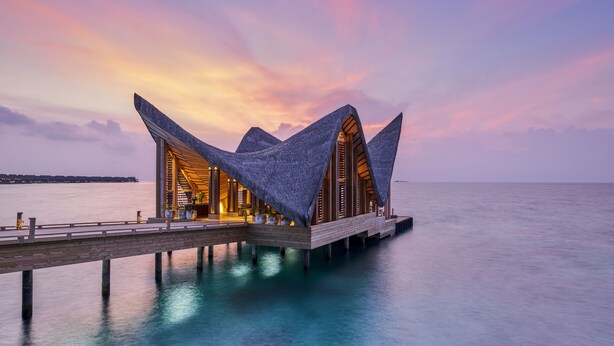 A modern resort with a unique architectural design featuring triangular roofs, situated on a wooden pier extending into calm waters. - JOALI Maldives (Muravandhoo)