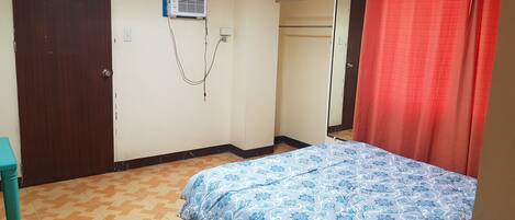 Un dormitorio con una cama, un televisor montado en la pared, un equipo de aire acondicionado y una cortina roja.