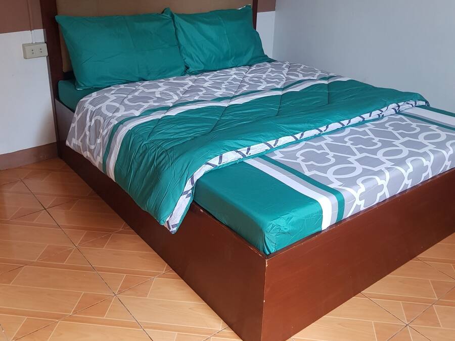 Een bed met een bedovertrek met patroon en twee kussens, een houten hoofdbord en een betegelde vloer.