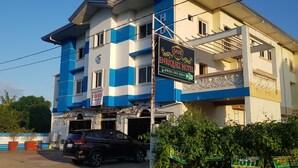 Un hôtel à la façade bleue et blanche, une enseigne indiquant « Hôtel Enriquez », et un VUS garé devant.