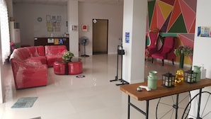 Un hall d’hôtel comprenant un comptoir d’accueil, un ensemble de canapés rouges, une petite table agrémentée d’objets décoratifs et un mur aux couleurs vives.