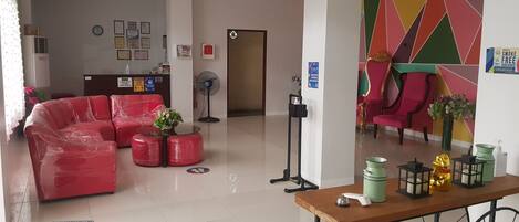 A hotel lobby with a reception desk, a red sofa set, a small table with decorative items, and a colorful wall design.